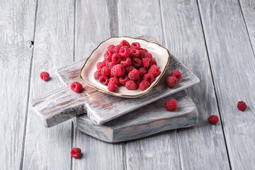 Raspberry fruits in plate on old cutting board, healthy pile of summer berries on grey wooden background, angle view