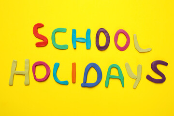 Phrase School Holidays made of modeling clay on yellow background, top view