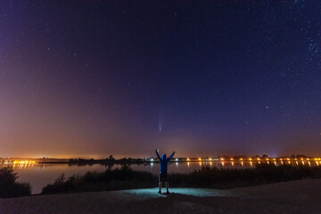 Fototapeta na wymiar Comet NEOWISE in the night sky over the river, with the Milky Way and a tourist with a tent