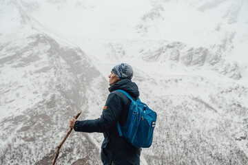 Back view selective focus portrait of adult male backpacker standing in mountainous landscape....