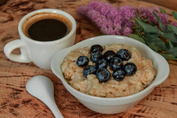 Oatmeal with blueberries for breakfast with coffee on a wooden table. Traditional healthy breakfast. Oatmeal and espresso. Close-up
