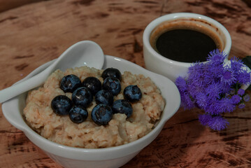 Oatmeal with blueberries for breakfast with coffee on a wooden table. Traditional healthy breakfast. Oatmeal and espresso. Close-up