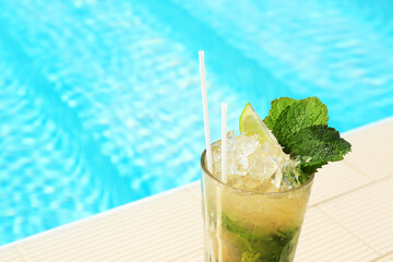 Glass of delicious mojito near swimming pool, space for text. Refreshing drink