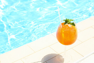 Glass of delicious cocktail near swimming pool, space for text. Refreshing drink
