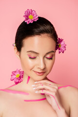 Fototapeta na wymiar naked beautiful woman with closed eyes, pink lines on body and flowers in hair isolated on pink