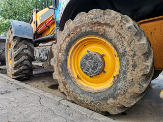 Close-up of a large wheel of a yellow excavator. Dirty rear wheel of an excavator. Construction...