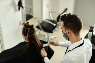 Hairdresser with protective face mask treating woman's hair at the salon during virus epidemic.