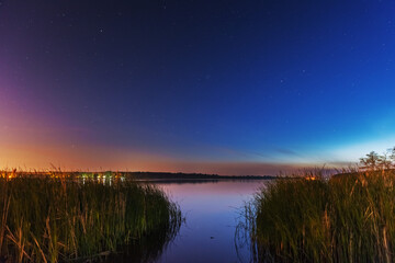 Comet NEOWISE in the night sky over the river, with the Milky Way and a tourist with a tent