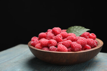 Delicious fresh ripe raspberries in plate on blue wooden table