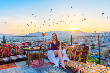 A woman have breakfast on one of the Cappadocia roof in early morning sunrise, when balloons fly....