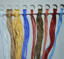 Organizer for mouline cotton threads with multicoloured threads for cross-stitch embroidery against white canvas. Closeup. Hobby. DIY. 