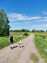 Fototapeta premium A man with a backpack on his back and a girl with a toy are walking along the road in the field