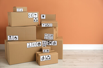 Cardboard boxes with different packaging symbols on floor near orange wall, space for text. Parcel delivery