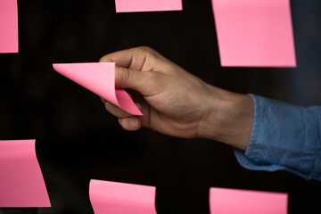 Close up of male arm tearing away sticky pink paper note from board. Concept of teamwork, chance, work at home, CEO, art director, idea, solution