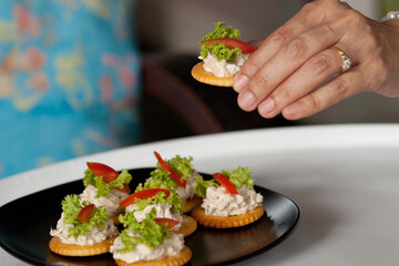 Chef is putting Tuna salad with crackers on black dish for serving at the party. Canape Tuna. Selective focus and blurred background.