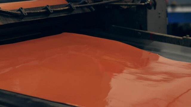 Close up of brown leather being coated on machine in factory