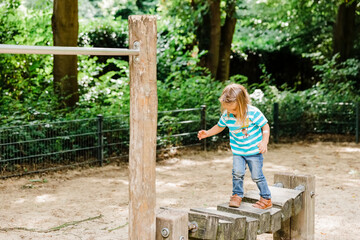 Obraz na płótnie Canvas Toddler girl walking on wooden playground equipment