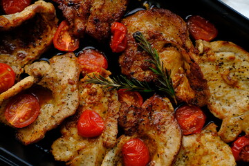 Homemade portions of pork baked in the oven with rosemary and tomatoes

