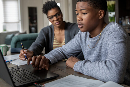 Mother helping teen son with college applications at dining table