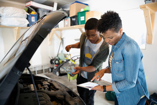 Mother And Son With Digital Tablet Changing Oil On Car In Garage