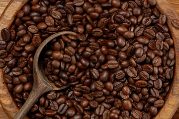 Coffee beans on a wooden spoon in a wooden bowl.