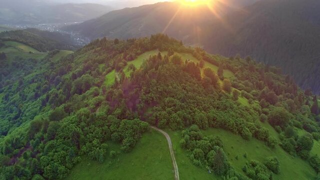 Nature landscape of flying above summer mountains during sunset. Hiking route. Sun hiding behing mountain covered with forest. Aerial shot, 4K