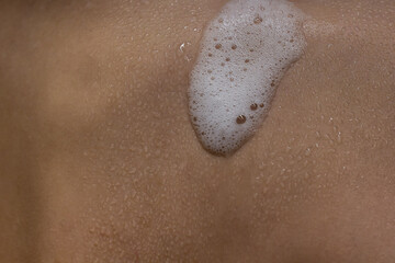 Close-up of shower foam and water drops on human skin. 