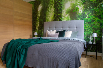 Bed with grey bedding, green blanket against a djungle photo wallpaper