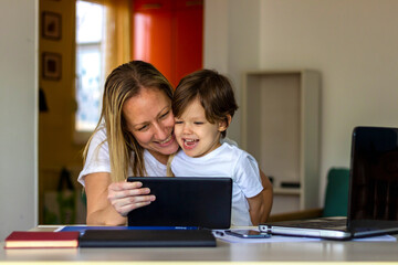 Fototapeta na wymiar Shot of young mother and adorable little son using tablet at home.Happy mom and little boy using tablet with touchscreen together watching video.Smiling mother and cute boy playing on digital tablet.