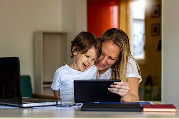 Shot of young mother and adorable little son using tablet at home.Happy mom and little boy using tablet with touchscreen together watching video.Smiling mother and cute boy playing on digital tablet.