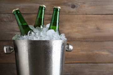Metal bucket with beer and ice cubes on wooden background, closeup. Space for text