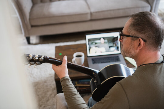 Man taking online guitar lessons at laptop in living room