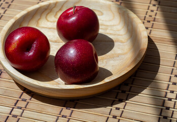 Red summer plums on a wooden and bamboo napkin in the sunlight