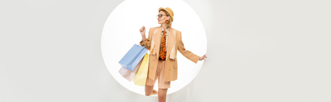 Horizontal image of smiling woman holding shopping bags near round hole on white background