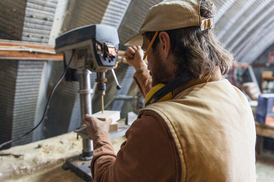 Male carpenter using drill press in woodworking workshop