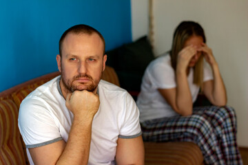 Cropped shot of an unhappy young couple after fight at home.Man looking worried while his wife is sad in the background.Young couple having an argument in their bedroom at home.Partners having issues.