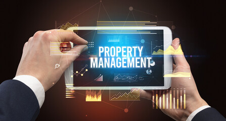 Close-up of hands holding tablet with PROPERTY MANAGEMENT inscription, modern business concept