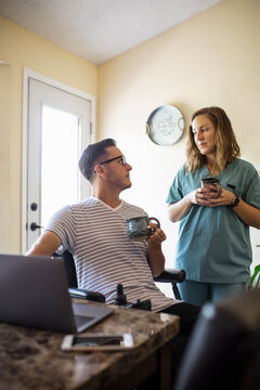 Quadriplegic man using laptop talking to medic girlfriend in scrubs
