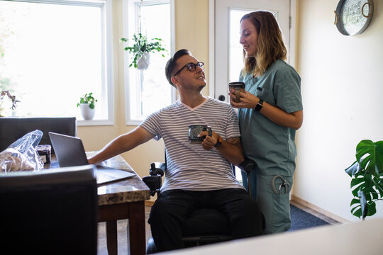 Quadriplegic man and medic girlfriend in scrubs looking at laptop