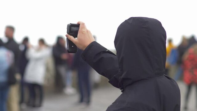 Young tourist man holding up action camera and taking picture against blurred faces of crowd - cliffs of Moore, Ireland
