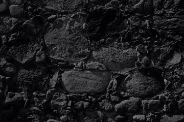 Black background. An old stone wall made of boulders and stones of different sizes in black color. Black and white photo. Monochrome.