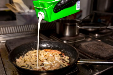 The cook adds cream to the pasta, which he warms in a black pan