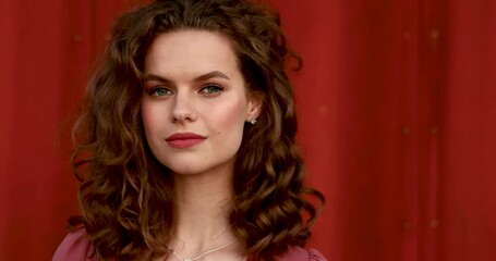 Confident young lady with beautiful makeup and hairstyle looking at camera with penetrated glance. Isolated over red background.