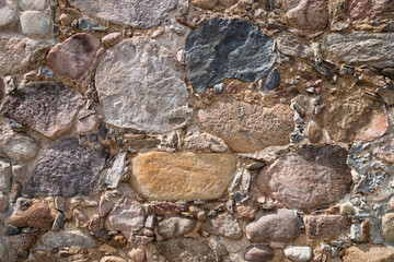 An old stone wall made of boulders and stones of different sizes.