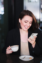 happy smiling young woman sitting at table in cafe looking cellphone - 367609113