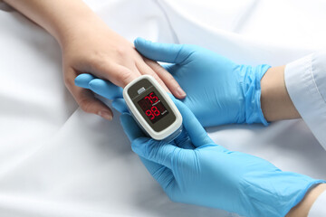 Doctor examining patient with fingertip pulse oximeter in bed, closeup