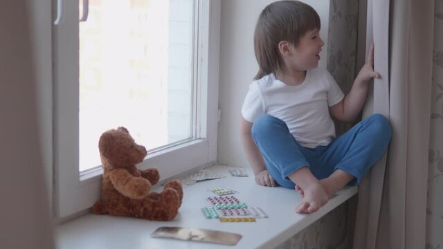 Toddler sits on windowsill and plays with scattering pills without parent's control. Dangerous situation with little boy. Medicines are freely available to child.