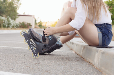 Blonde girl in a white blouse, jeans and skates tying her laces. Roller-skating concept