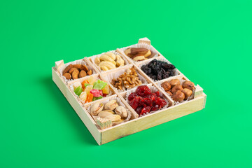 Assorted dried fruits and nuts in a wooden box isolated on a green background. Raisins, candied fruits, cherries, Brazil nuts, hazelnuts, walnuts, almonds, cashews, pistachios.