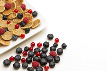 Blueberries and raspberries with pancakes in white bowl. Berries on table. White background